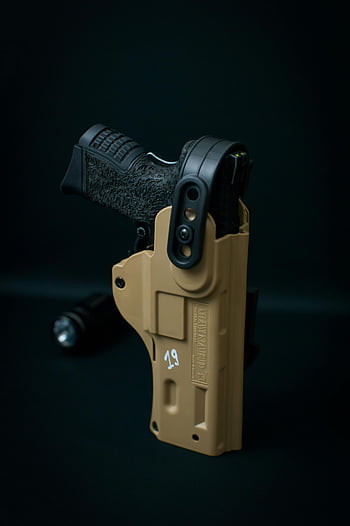 close-up shot, black pistol, tan holster, dark background, handgun, firearm, tactical accessory, outdoor equipment, safety gear, firearm accessory, concealed carry holster
