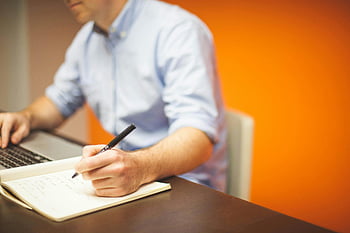 muž psaní, laptop, moderní kancelář, lavice, zaostřovací fotografie, poznámky, pero, pracovní prostředí, Profesionální nastavení, oranžové pozadí, produktivita