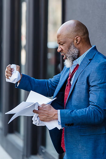 angry businessman, crumpled paper, city street, frustrated businessman, stress, dissatisfaction, professional man, outdoor scene, business attire, emotional expression, urban setting