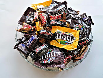M&Ms, clear cut glass bowl, chocolate candies, Twix, Snickers, vibrant dessert spread, candy bowl, assorted chocolates, sweet treats, dessert display, candy assortment