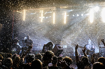 Koncert živé hudby, Jevištní umělci, nadšené publikum, Světlá jevištní světla, Dynamická koncertní scéna, hudební událost, Koncertní atmosféra, představení, živé vystoupení, koncert davu, scénické osvětlení