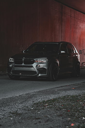 BMW X5, black SUV, parked, under bridge, dramatic lighting, modern design, red wall, stylish car, urban setting, vehicle photography, automotive design