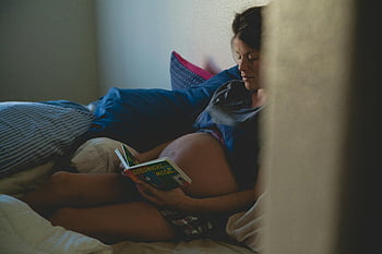 schwangere Frau, Buch lesen, auf dem Bett sitzen, ruhiger Moment, intimer Moment, Schwangerschaft, Bettruhe, Mutterschaft, Gemütliche Szene, Entspannung