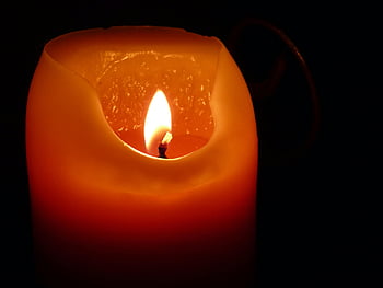 orange candle, candle flame, warm glow, close-up shot, candlelight, darkness, illumination, orange wax, candle wick, candle holder, ambient light