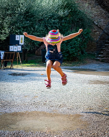 ragazza che salta, bambino che salta, scena del parco, San Gimignano Italia, giorno soleggiato, Scena vibrante, attività all'aperto, momento giocoso, Cappello colorato, sentiero di ghiaia, bambino gioioso