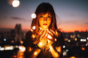 Donna che tiene lucciole, ritratto romantico, luci a corda luminosa, skyline della città, crepuscolo, effetto bokeh, Scena della notte urbana, illuminazione calda, fotografia all'aperto, soggetto femminile, Atmosfera serale