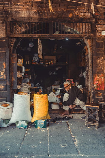 elderly merchant, traditional market, Pakistan, bags of goods, store interior, market setting, sitting man, goods bags, market goods, traditional store, elderly man