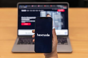 smartphone, Hexnode-appen, närbild skott, hålla handen, suddig bärbar dator, mobilenhet, teknologi, appvisning, digital skärm, kontorsinställning, arbetsmiljö