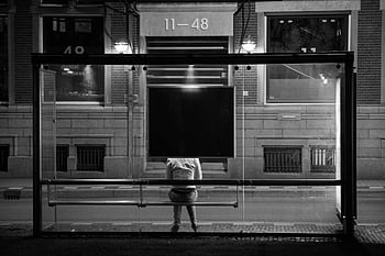 grayscale photography, person sitting, bus stop, night scene, urban life, solitude, black and white, street photography, cityscape, nighttime, lone figure