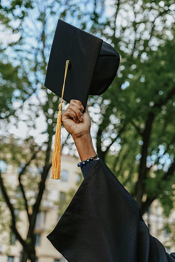 graduation hat, black graduation cap, hand holding, celebration, trees, close-up, graduation day, academic achievement, outdoor celebration, tassel, graduation gown