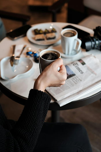 main tenant une tasse de café, scène confortable, collations de table, journal, l'heure du café, routine matinale, table de petit déjeuner, pause café, moment de détente, CAFE RÉGLAGE, tasse à café