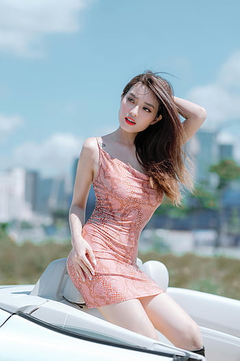 pink spaghetti strap dress, white convertible, cityscape backdrop, stylish woman, confident pose, outdoor fashion, urban setting, summer style, modern fashion, car photography, female model