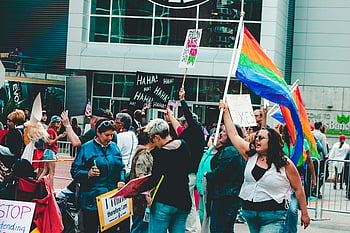LGBTQ pride rally, colorful flags, diverse people, creative signs, pride parade, rainbow flags, protest signs, urban event, community gathering, public demonstration, building front