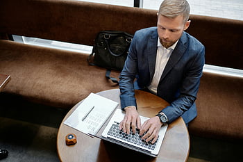 man in suit, typing on laptop, overhead view, round table, business setting, professional attire, office environment, work scene, focused individual, modern workspace, businessperson working