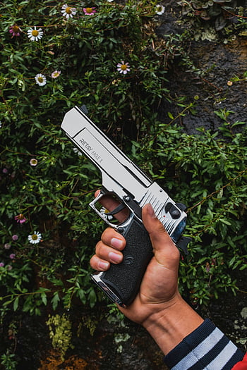 hand holding gun, silver pistol, nature background, security contrast, outdoor setting, Retay Eagle X, floral backdrop, greenery, close-up shot, human hand, firearm display