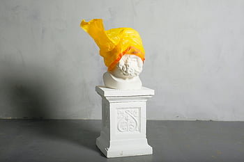 classical marble bust, yellow plastic bag, vibrant yellow plastic, striking visual statement, marble sculpture, plastic-covered sculpture, artistic statement, contemporary art, modern art, yellow plastic art, marble bust art