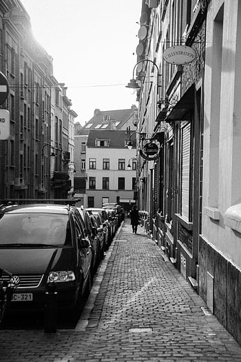 grayscale photography, parked cars, side of road, monochrome urban street, vintage buildings, timeless charm, cobblestone street, street signs, building facades, street lamps, parked vehicles