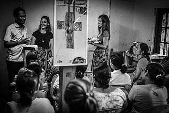 educational seminar, diverse group, people gathering, room, white framed rectangular mirror, cross, black and white, audience, speaker, presentation, chairs