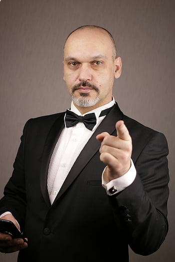 رجل يرتدي بدلة سوداء،  رجل أصلع،  سهرة،  مشيرا إلى الكاميرا،  إعداد الاستوديو،  رجل واثق،  ربطة القوس،  جوال،  بالزي الرسمي،  صورة احترافية،  التصوير الفوتوغرافي في الاستوديو