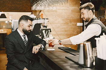 ワイングラスを持った男性、 飲み物を提供するバーテンダー、 ビジネスクライアント、 スタイリッシュなバーカウンター、 バーの雰囲気、 プロの服装、 ドリンクサービス、 バーインタラクション、 エレガントなバーの雰囲気、 フォーマルなビジネスの服装、 バーカウンターでの交流