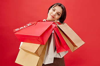 woman, short hair, holding shopping bags, cheerful, sale, red background, multiple shopping bags, shopping, sale sign, red shopping bag, brown shopping bag