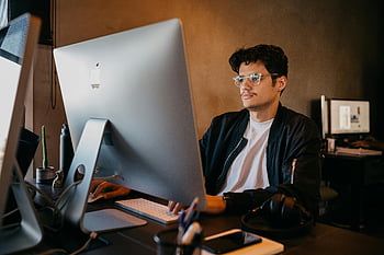 man in eyeglasses, sitting in office, working, desktop computer, modern decor, focused on work, office environment, man working, computer work, office worker, modern office