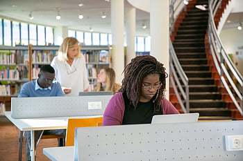 rozmanité studenti, Moderní univerzitní knihovna, soustředěné učení, notebooky, pečlivé studium, skupinové studium, vzdělávací prostředí, Studie knihovny, mladí studenti, Akademické prostředí, Zaměřené učení