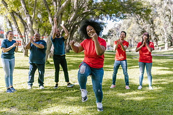group cheering, woman in red shirt, team building game, outdoor activity, friendship, motivation, joyful group, park setting, team spirit, group engagement, outdoor fun
