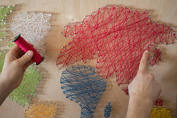 string art, colorful threads, wooden board, vibrant threads, hands creating, string art map, world map, craft project, DIY art, artistic design, thread art