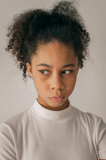 Bekymret sort pige, teenager med krøllet hår, eftertænksom look, indendørs, isoleret på hvid baggrund, nær væg, sort pige portræt, krøllet hår, eftertænksomt udtryk, indendørs portræt, hvid baggrund
