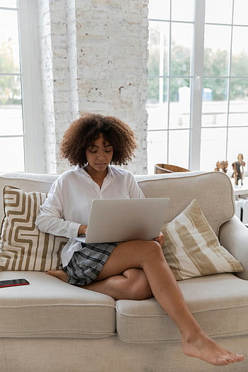 donna afroamericana, lavorare online, netbook, divano accogliente, soggiorno luminoso, ufficio a casa, signora focalizzata, il computer portatile, Lavoro casuale, impostazione interna, Spazio di lavoro confortevole