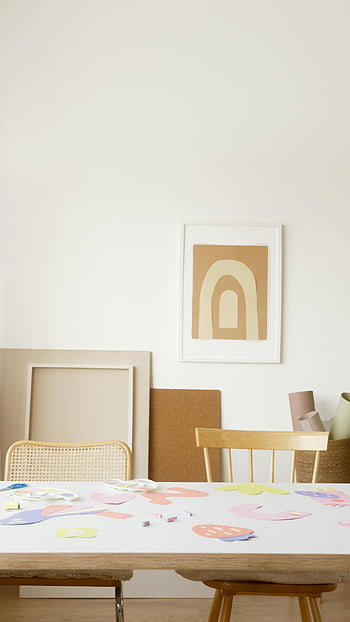 artworks on white table, colorful paper cutouts, artistic wall decor, creative art studio, abstract art, framed artwork, white table, studio setup, art supplies, wooden chairs, wall art
