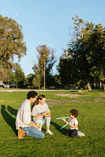 family playing outdoors, sunny park, happy family, couple with kid, outdoor play, grassy field, trees in background, family fun, playful moment, park activities, family togetherness