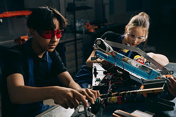 electric engineers, robotic equipment, workshop setting, young engineers, safety goggles, technical work, engineering project, hands-on work, mechanical components, collaborative work, technology development