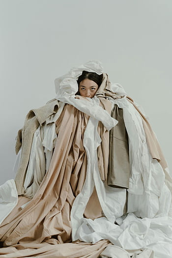 Asian woman, covered with clothes, neutral-toned clothes, layers of clothing, partially hidden, fashion photography, creative portrait, studio shot, minimal background, artistic composition, textile textures