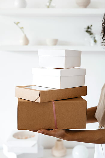 hromada krabic, Elegantní dárkové boxy, Minimalistické vnitřní nastavení, Osoba, která drží krabice, Bílé dárkové krabice, hnědé kartonové krabice, detailní záběr, fotografování v interiéru, dárkové balení, moderní interiér, čisté pozadí