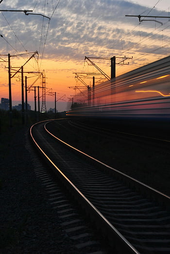 Ferrovia, cielo grigio e arancione, tramonto, treno sfocato, Tracce curve, tramonto vibrante, scatto dinamico, rotaie, pali elettrici, sfocatura movimento