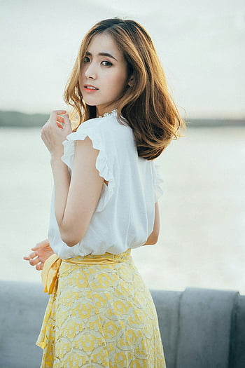 woman by water, white sleeveless shirt, yellow floral skirt, waterside portrait, elegant style, charming young woman, outdoor fashion, summer outfit, fashion by water, stylish woman, waterside elegance