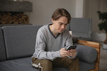 Mies, jolla on harmaa villapaita, nuorimies, harmaa sohva, älypuhelimen käyttäminen, sisällä, mukava istuu, Rento asu, olohuone, rento asento, kotiympäristö, moderni elämäntapa