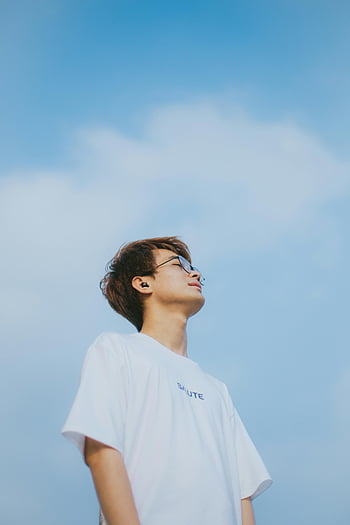 junger asiatischer Mann, weißes T-Shirt, Brille, Serene Porträt, strahlend blauer Himmel, hoch schauen, Foto im Freien, Lässiger Kleidungsstil, Friedlicher Ausdruck, klarer Himmel, natürliches Licht