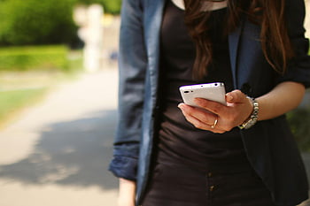 Frau hält Smartphone, weißes Smartphone, Sunny Day im Freien, Nahaufnahmefrau, im Freien gehen, Smartphone -Nutzung, sonniger Tag, Outdoor-Szene, Frau mit Telefon, Lässige Kleidung, Smartwatch