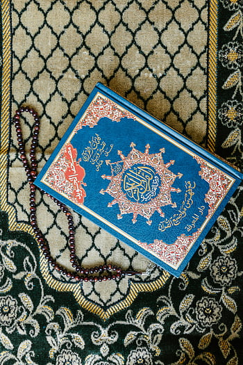 Quran, prayer beads, Islamic carpet, top view, decorative carpet, blue book, religious text, Islamic art, prayer accessories, holy book, cultural artifact