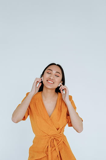 幸せな女、 オレンジドレス、 ワイヤレスイヤホン、 音楽を聴く、 笑顔の女性、 屋内写真、 音楽を楽しんでいます、 屋内設定、 オレンジの女性、 イヤホン