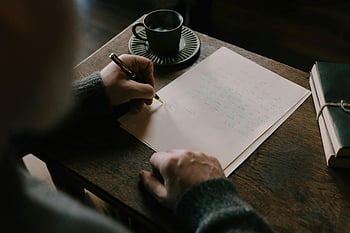 man writing letter, wooden desk, cup of coffee, warm atmosphere, intimate setting, adult writing, handwritten letter, cozy scene, pen and paper, book on desk, coffee cup