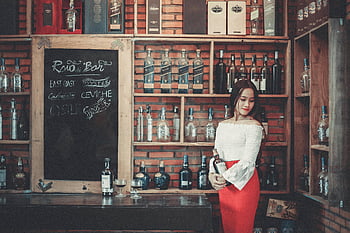 아시아 여자, 세련된 복장, 병을 들고, 소박한 바, 나무 선반, 알코올 음료, 바 세팅, 유행, 음료수, 바 메뉴, 붉은 치마