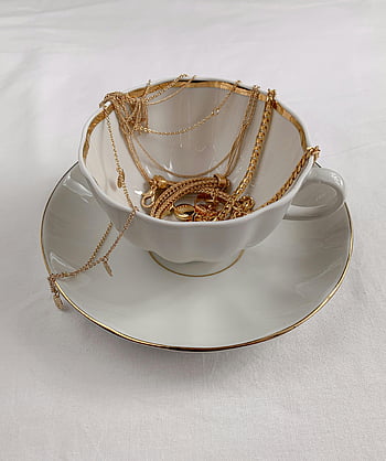 gioielli, tazza di tè, collane d'oro, braccialetti d'oro, tazza da tè in porcellana, piattino, display elegante, disposizione artistica, gioielli di classe, catene d'oro, sfondo bianco