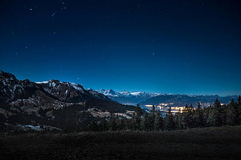 snowy mountain, nighttime landscape, starry night, illuminated town, mountainous backdrop, winter scenery, night photography, alpine view, night sky, snow-covered peaks, scenic night view