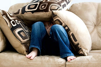kid hiding, pillows, child crouched, cushions, couch, playfulness, fear, indoor play, playful child, hiding game, cozy setting