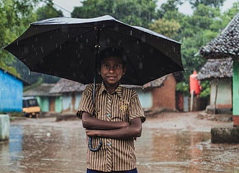 chlapec hospodářství deštník, černý deštník, deštivý den, vesnice scény, Odisha India, mladý kluk, venkovní fotografie, Venkovské prostředí, deštivé počasí, vesnický život, usměvavý chlapec
