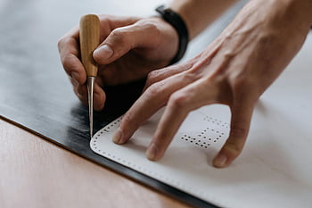 craftsmanship, chisel carving, manual marking, leatherworking, hand tools, precision crafting, close-up view, black material, artisan technique